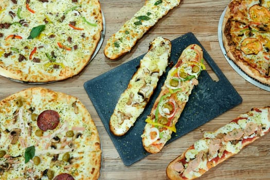 A variety of pizzas and breadsticks are displayed on a table. The pizzas are of different sizes and flavors, while the breadsticks are cut into smaller pieces