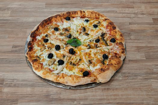 A pizza with olives and mushrooms on it. The pizza is sitting on a wooden table. The pizza is ready to be eaten
