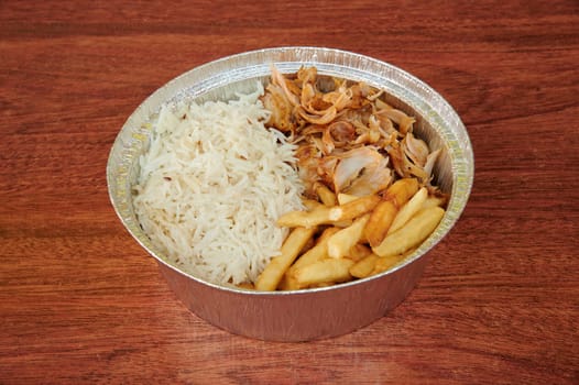 A bowl of food with rice, chicken, and french fries. The bowl is made of plastic and is sitting on a wooden table