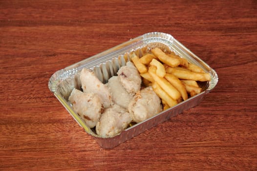 A tray of chicken and french fries sits on a wooden table. The chicken is cut into small pieces and the fries are golden brown. The presentation is simple and appetizing
