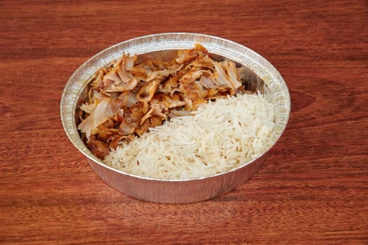A bowl of rice and meat on a wooden table. The bowl is covered in foil. The rice is white and the meat is brown