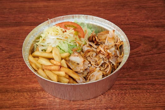 A bowl of food with a side of fries and a salad. The salad is topped with tomatoes and lettuce