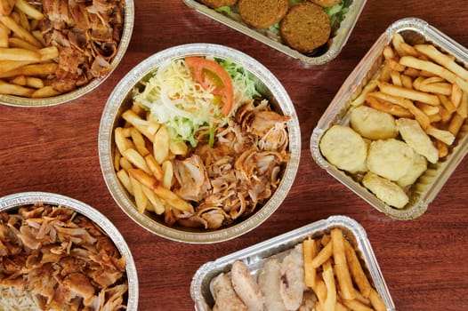 A variety of kebab items are displayed in aluminum trays, including chicken, fries, and other side dishes