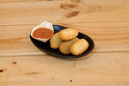 A plate of fried dough balls with a dipping sauce. The sauce is red and the dough balls are green and white
