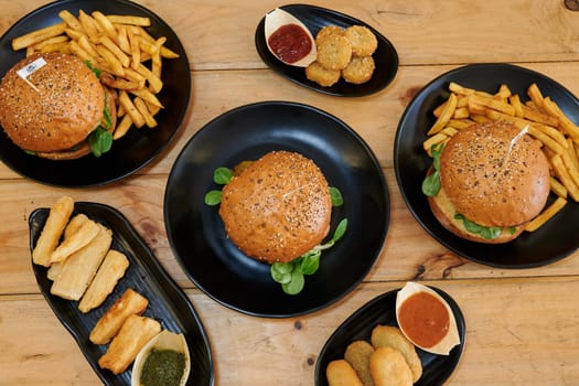 A table with a variety of food items including hamburgers, fries, and other snacks. The table is set up in a casual and inviting manner, with the food items arranged in different plates and bowls