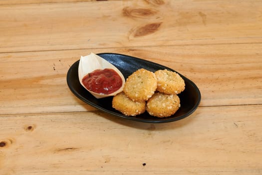 A plate of fried chicken with a dipping sauce and a wooden table. Scene is casual and relaxed