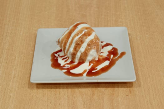 A dessert with a white and brown sauce drizzled on top is placed on a white plate. The dessert is a delicious treat that is perfect for satisfying one's sweet tooth. The combination of the white