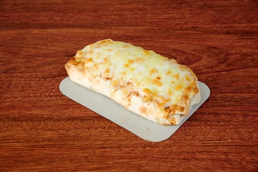 A piece of pizza with cheese on top of a wooden table. The pizza is cut in half and placed on a paper plate