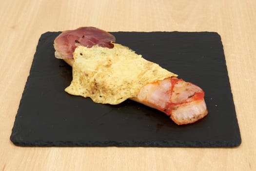 A plate of food with bacon and cheese on top of a black plate. The bacon is cooked and the cheese is melted. The plate is on a wooden table