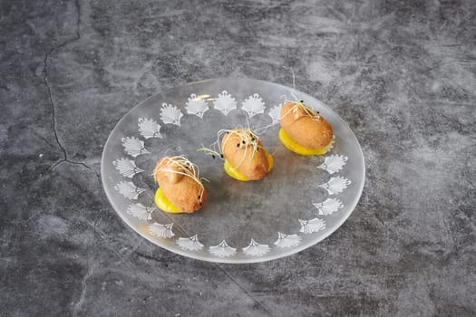 Three small fried dough balls are on a white plate with a pattern. The plate is placed on a grey surface