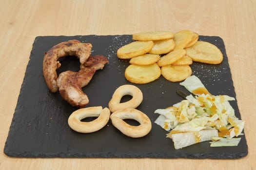 A plate of food with a variety of items including meat, potatoes, and vegetables. The plate is on a wooden table