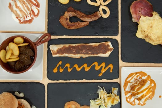 A variety of food items are displayed on a black table, including sandwiches, meat, and vegetables. The presentation is colorful and appetizing, with a mix of textures and flavors