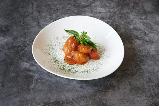 A plate of food with a green leaf on top. The plate is white and the food is red
