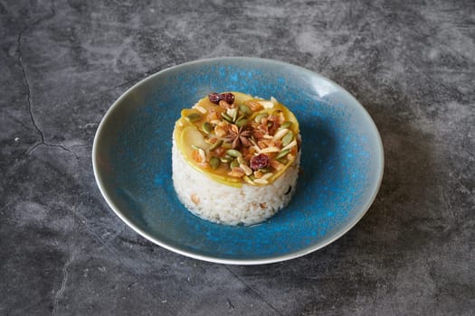 A blue plate with rice and nuts on it. The plate is on a grey surface. The rice is surrounded by nuts and there is a small piece of fruit on the plate
