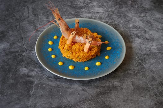 A plate of food with shrimp on top of a rice dish. The plate is blue and the shrimp are arranged in a way that they look like they are laying on top of the rice