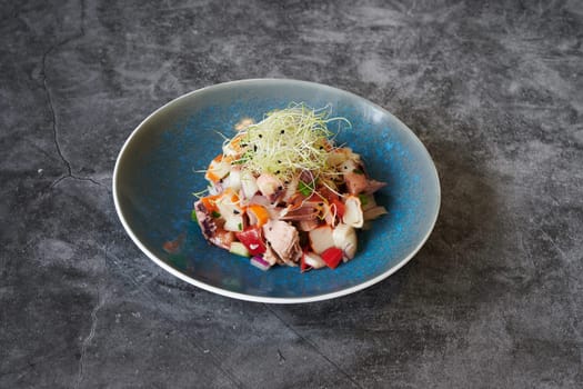 A blue plate with a salad on it. The salad is topped with green sprouts. The plate is placed on a grey surface