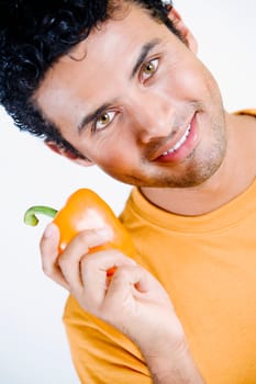 Portrait of a young man holding an orange bell pepper and smiling