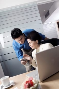 Businesswoman sitting in front of a laptop with a businessman holding a mobile phone standing behind her