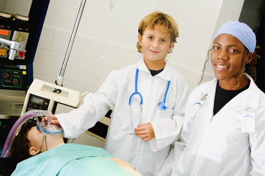 Boy imitating a doctor and adjusting the oxygen mask of a patient with a female doctor standing beside him