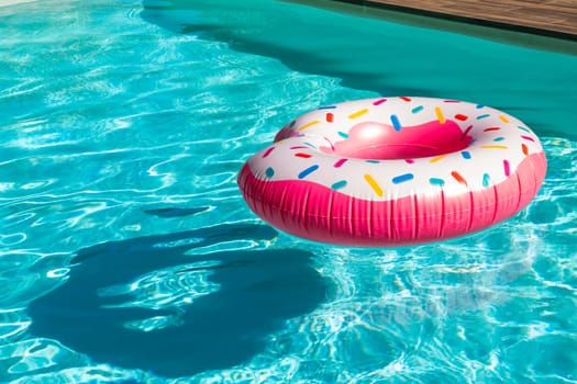 Pink donut-shaped inflatable float in turquoise swimming pool with shadow and wooden deck
