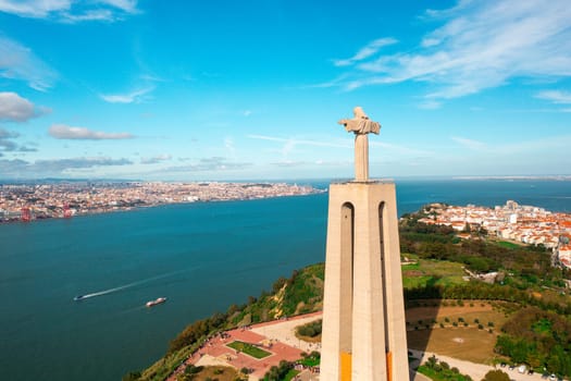 Aerial drone view of monument Sanctuary of Christ the King. Majestic scenery statue overlooking cityscape Almada and Tagus River. Bird's eye view of Catholic monument and city