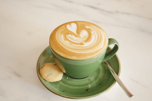 A beautifully crafted latte with foam art and a cookie on the side.