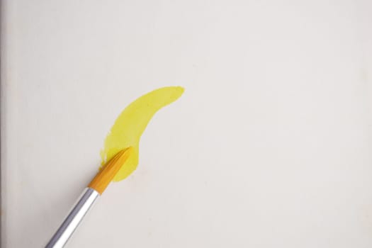 A brush applies a bright yellow paint stroke on white canvas.