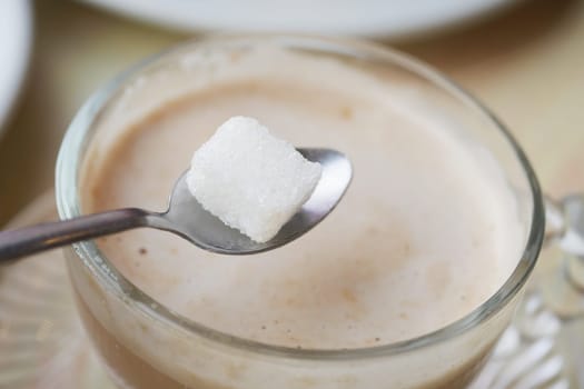 A spoon holds a sugar cube over a warm, frothy drink at a cafe.