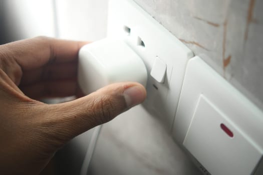 A person connects a charger to a power socket in their living space.