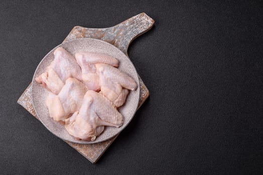 Raw chicken wings with salt, spices and herbs on a wooden cutting board on a dark concrete background