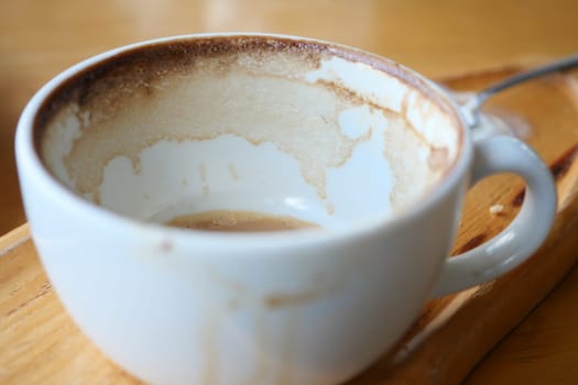 Cup sits empty on a wooden tray, showing the traces of a recent drink.
