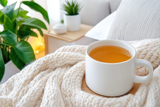 A white ceramic cup of herbal tea on a wooden tray, wrapped in a chunky knit blanket, surrounded by soft pillows and green plants, creating a relaxing and warm atmosphere