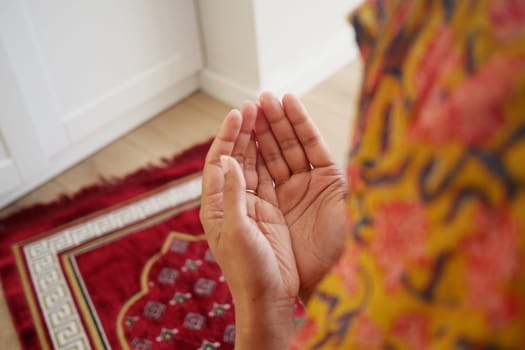 Hands are positioned for prayer on a vibrant rug in a peaceful space.