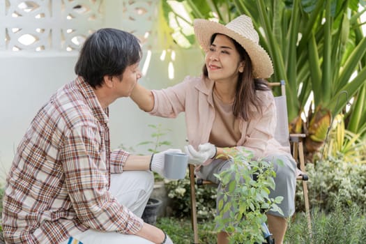 An elderly Asian woman affectionately touching her partner's face while they enjoy gardening together, surrounded by lush greenery.