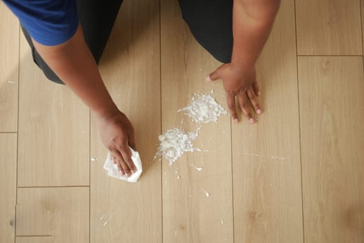 Person kneels, cleaning a white spill with a cloth.