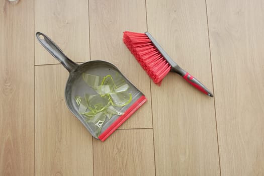Shards of broken glass are being cleaned up with a dustpan and brush.