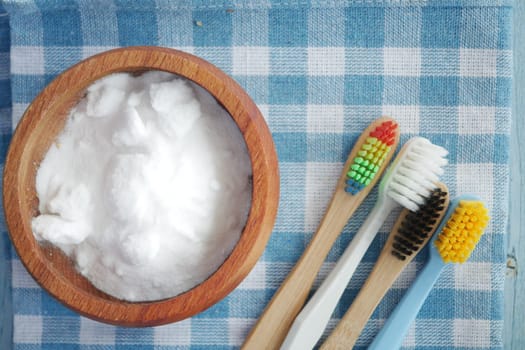 Baking soda in a wooden bowl with colorful toothbrushes for whitening.