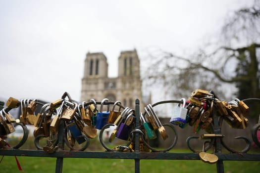Close-up of colorful love locks attached to a fence in Paris, France 20.01.202, with the blurred towers of Notre Dame Cathedral in the background.
