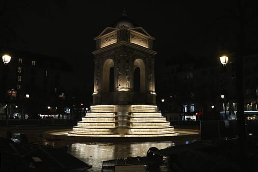 Night view of a beautifully lit historical fountain and monument in Paris, France 20.01.202, surrounded by streetlights in an urban setting.