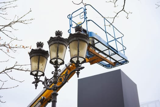 Close-up of an ornate vintage street lamp in Paris, with a construction lift in the background against an overcast sky