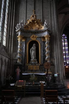 A detailed view of a religious altar featuring a marble statue of Mary, ornate golden decorations, and floral offerings in a Gothic cathedral. Amiens. France 17.02.2025