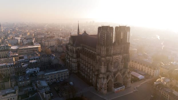 Aerial view of the majestic Reims Cathedral in France, illuminated by golden sunrise light. The iconic Gothic landmark is surrounded by the urban cityscape of Reims.