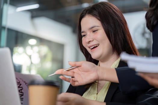 A businesswoman expresses joy while collaborating on analysis and planning with a colleague, reviewing documents and a laptop in a contemporary office environment.