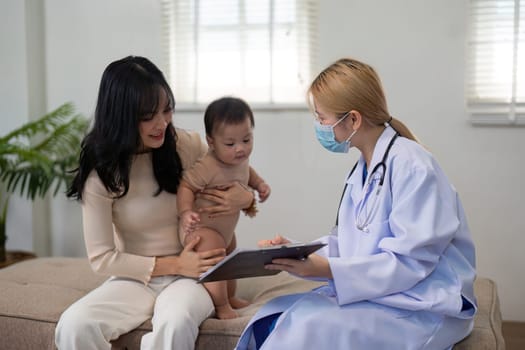 A pediatric doctor discusses health information with a parent while the parent holds their baby in a welcoming clinic environment.