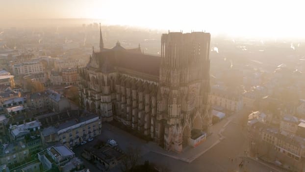 Aerial view of the Reims Cathedral in France during a golden sunrise. The Gothic masterpiece stands amidst the historic cityscape, exuding elegance and heritage.