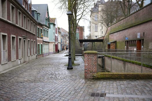 A cobblestone street in Amiens, France, lined with colorful shuttered houses, brick walls, vintage lampposts, and a serene canal, creating a historic charm