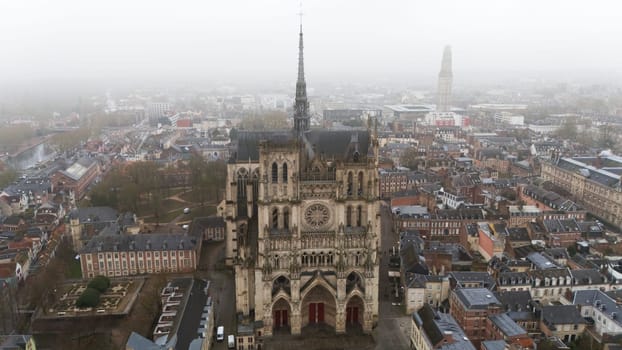 Aerial view of the Gothic Amiens Cathedral in northern France, surrounded by historic buildings and a foggy urban cityscape. A stunning UNESCO World Heritage landmark