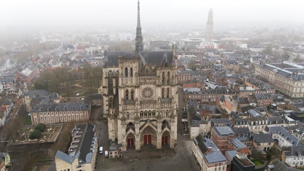 Aerial Front View of Amiens Cathedral, a UNESCO Gothic Landmark, Surrounded by Historic and Foggy Cityscape in Northern France.