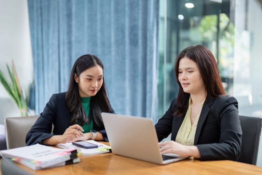 Two professional women utilize digital devices to conduct project analysis and planning, showcasing teamwork and innovation in a modern office environment.