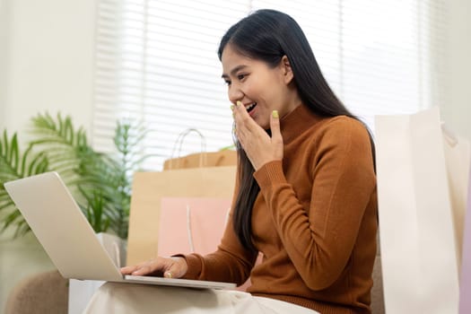 A delighted woman is engaged in online shopping, holding her credit card and smiling with excitement at her successful transaction.
